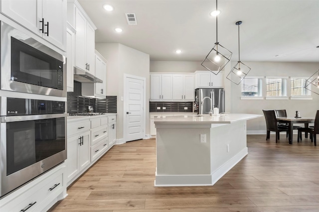kitchen featuring stainless steel appliances, under cabinet range hood, decorative backsplash, baseboards, and light countertops