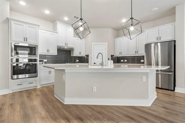 kitchen featuring stainless steel appliances, a sink, tasteful backsplash, under cabinet range hood, and light countertops