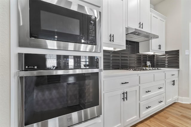kitchen with stainless steel appliances, light countertops, backsplash, under cabinet range hood, and white cabinetry
