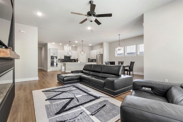 living room with a ceiling fan, baseboards, light wood-style floors, recessed lighting, and a chandelier