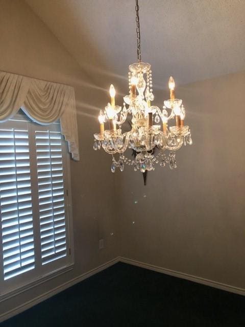 empty room with a chandelier, lofted ceiling, and baseboards