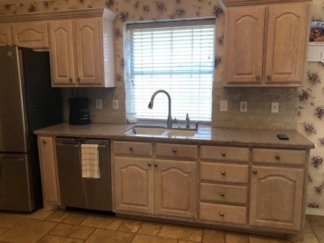 kitchen with appliances with stainless steel finishes, a sink, wallpapered walls, backsplash, and baseboards