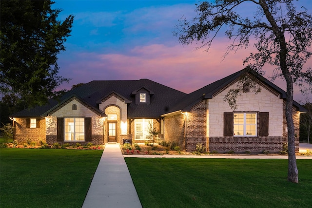french country style house with a front yard, stone siding, and brick siding