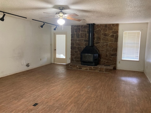 12735 County Road 2922, Eustace, TX 75124 - unfurnished living room featuring a textured ceiling, track lighting, wood finished floors, a ceiling fan, and a wood stove