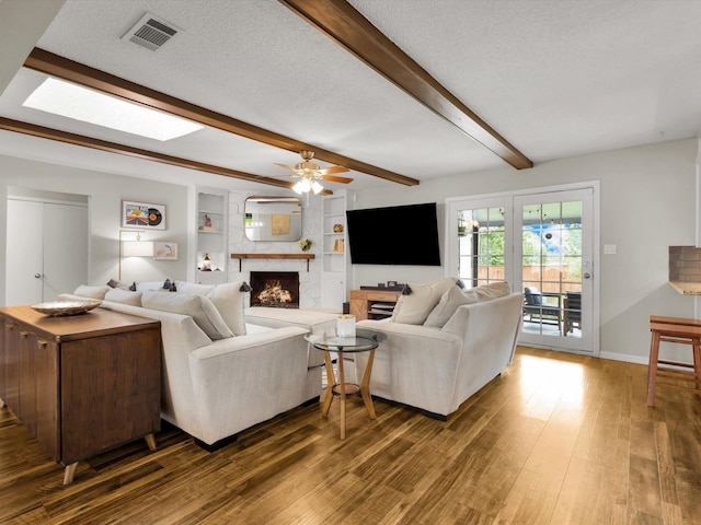 living area with a ceiling fan, wood finished floors, beamed ceiling, a lit fireplace, and baseboards