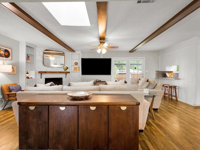 living room with ceiling fan, beamed ceiling, a fireplace, dark wood-type flooring, and baseboards