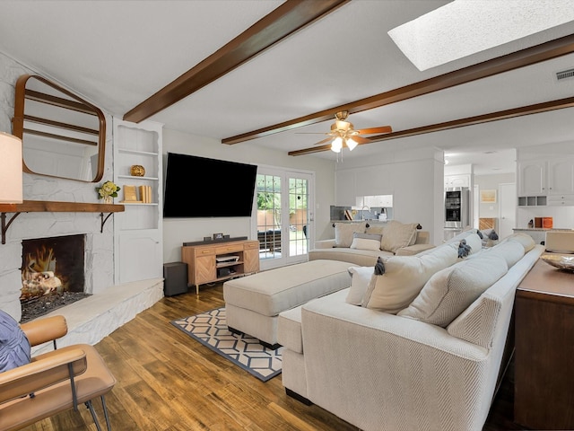 living area featuring wood finished floors, a skylight, a premium fireplace, beam ceiling, and a ceiling fan