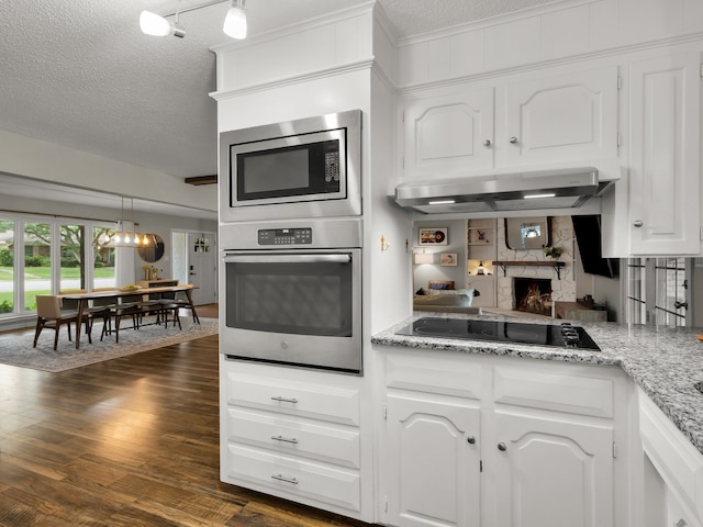 kitchen featuring appliances with stainless steel finishes, under cabinet range hood, a textured ceiling, white cabinetry, and a high end fireplace