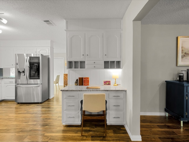 kitchen with stainless steel fridge, a textured ceiling, wood finished floors, white cabinetry, and light stone counters
