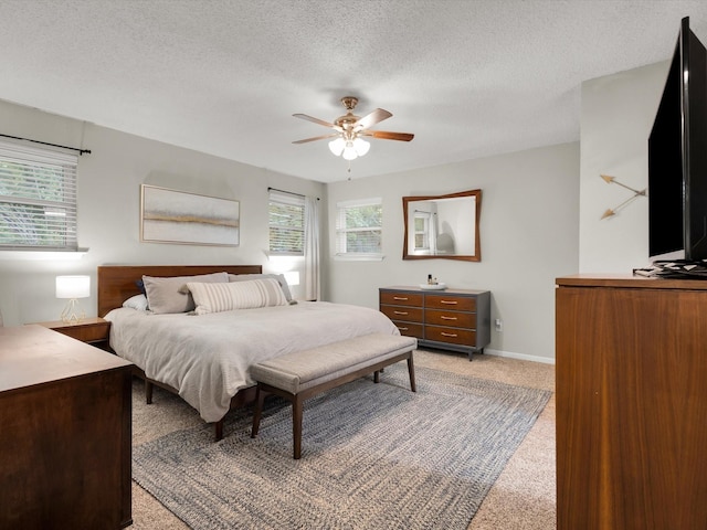bedroom featuring light colored carpet, a textured ceiling, ceiling fan, and baseboards