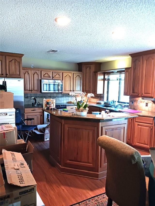 2435 St Gregory St, Arlington, TX 76013 - kitchen featuring stainless steel appliances, a textured ceiling, dark wood finished floors, decorative backsplash, and a kitchen island