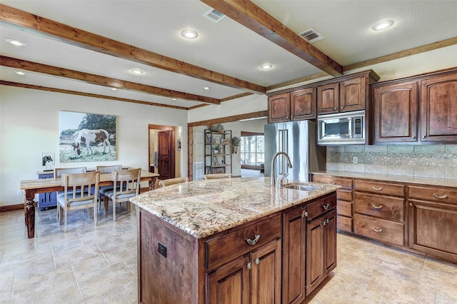 kitchen featuring appliances with stainless steel finishes, a sink, beamed ceiling, decorative backsplash, and an island with sink