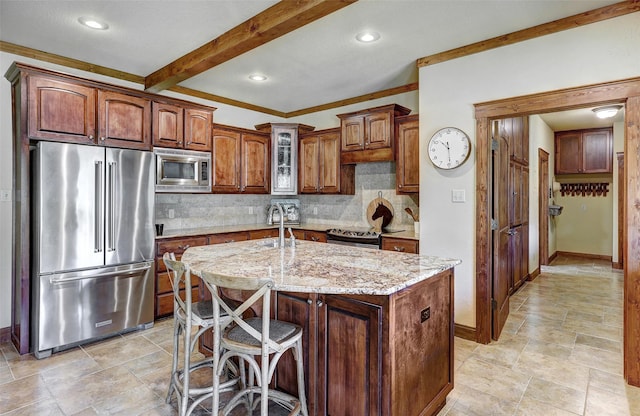 kitchen with appliances with stainless steel finishes, backsplash, light stone counters, an island with sink, and baseboards