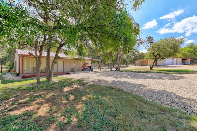 view of yard featuring driveway, a garage, fence, and an outbuilding