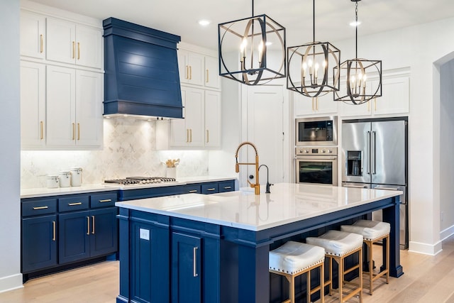 2200 Sandalwood Dr, Prosper, TX 75078 - kitchen with appliances with stainless steel finishes, blue cabinetry, custom range hood, a chandelier, and light wood finished floors