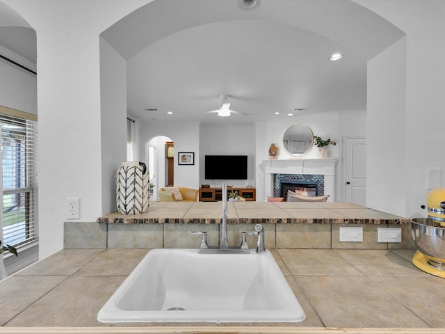 1806 Briarcrest Ln, Arlington, TX 76012 - kitchen with a sink, a ceiling fan, a fireplace, arched walkways, and tile counters