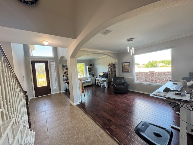entryway with arched walkways, crown molding, plenty of natural light, baseboards, and wood finished floors