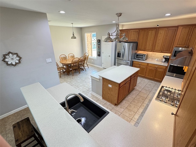 kitchen featuring appliances with stainless steel finishes, a sink, brown cabinets, light tile patterned flooring, and a center island