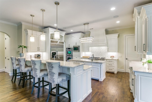 kitchen featuring built in appliances, a peninsula, arched walkways, tasteful backsplash, and crown molding
