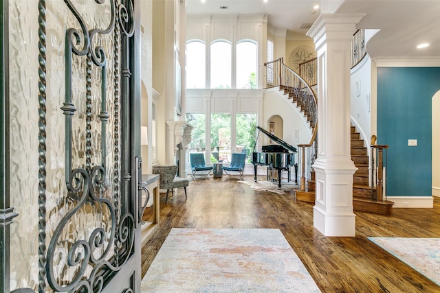 foyer with stairs, wood finished floors, ornamental molding, decorative columns, and a towering ceiling