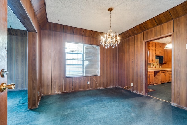 spare room featuring wood walls, carpet, a chandelier, and a textured ceiling