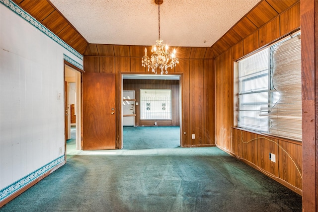 carpeted empty room featuring wood walls, a chandelier, and a textured ceiling