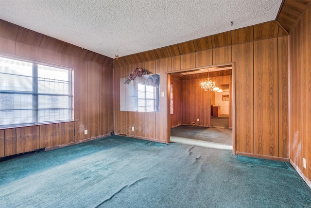carpeted spare room featuring a chandelier, a textured ceiling, and wood walls