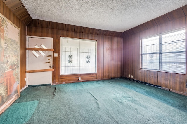 empty room with carpet floors, wooden walls, and a textured ceiling