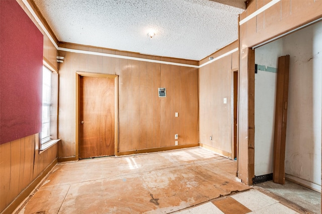 empty room with crown molding, wooden walls, and a textured ceiling
