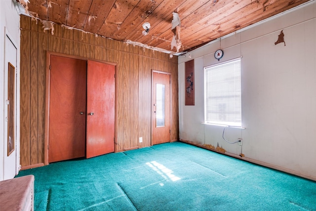 carpeted empty room with wood ceiling and wooden walls