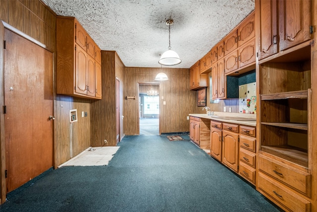 kitchen featuring brown cabinetry, dark colored carpet, wood walls, light countertops, and pendant lighting