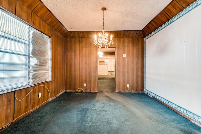 carpeted empty room with a chandelier, wooden walls, plenty of natural light, and a textured ceiling