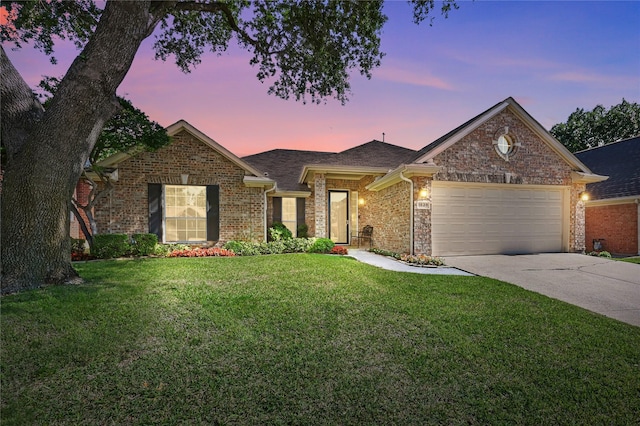 view of front of property featuring an attached garage, concrete driveway, a yard, brick siding, and roof with shingles