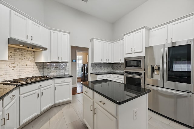 kitchen featuring stainless steel appliances, under cabinet range hood, white cabinets, a center island, and backsplash