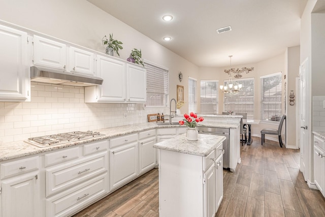 7013 Caldwell Ln, Plano, TX 75025 - kitchen with under cabinet range hood, a peninsula, appliances with stainless steel finishes, a chandelier, and white cabinetry