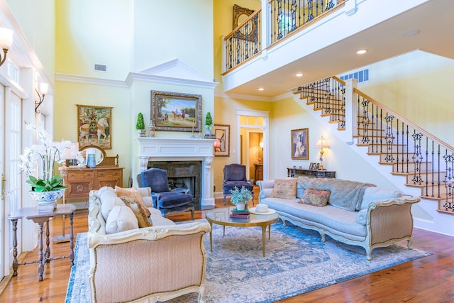 living room with a towering ceiling, stairs, a fireplace, ornamental molding, and wood finished floors