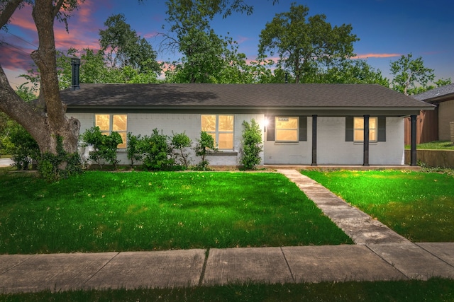 ranch-style home featuring a yard, brick siding, and roof with shingles