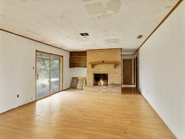 110 Twin Cir, Wortham, TX 76693 - unfurnished living room with light wood finished floors, a brick fireplace, wood walls, and ornamental molding