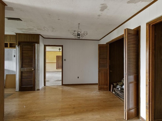 110 Twin Cir, Wortham, TX 76693 - empty room featuring crown molding, a chandelier, light wood finished floors, baseboards, and wood walls