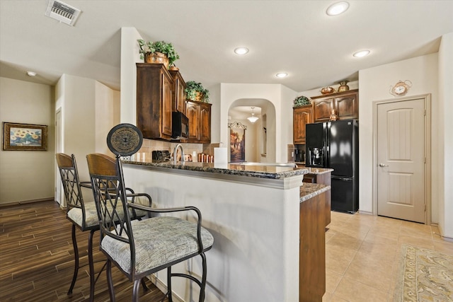 5139 Crystal Lake Ave, Krum, TX 76249 - kitchen with black appliances, arched walkways, dark stone counters, a peninsula, and a breakfast bar