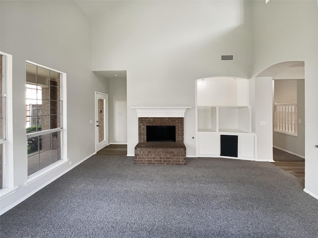 11473 Las Polamas Dr, Frisco, TX 75033 - unfurnished living room with a towering ceiling, dark carpet, a fireplace, arched walkways, and baseboards