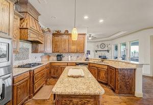 2575 Wincrest Dr, Rockwall, TX 75032 - kitchen featuring a peninsula, appliances with stainless steel finishes, a center island, brown cabinetry, and recessed lighting