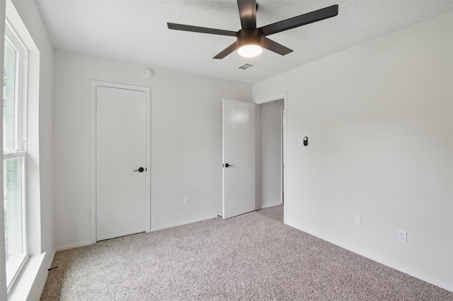 unfurnished bedroom featuring light colored carpet, multiple windows, a ceiling fan, and a textured ceiling