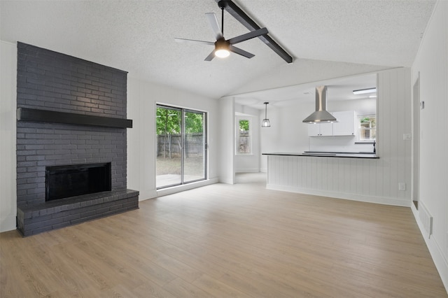 unfurnished living room featuring light wood finished floors, a ceiling fan, a brick fireplace, and a textured ceiling
