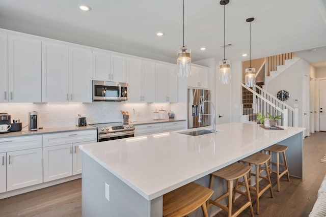 238 Estates Cir, College Station, TX 77840 - kitchen with appliances with stainless steel finishes, wood finished floors, a center island with sink, a sink, and backsplash