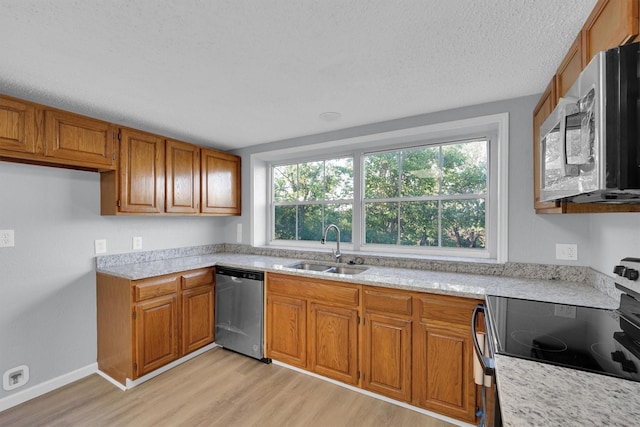 3355 La Mesa Dr, Weatherford, TX 76085 - kitchen featuring stainless steel appliances, a sink, brown cabinets, light wood finished floors, and a textured ceiling