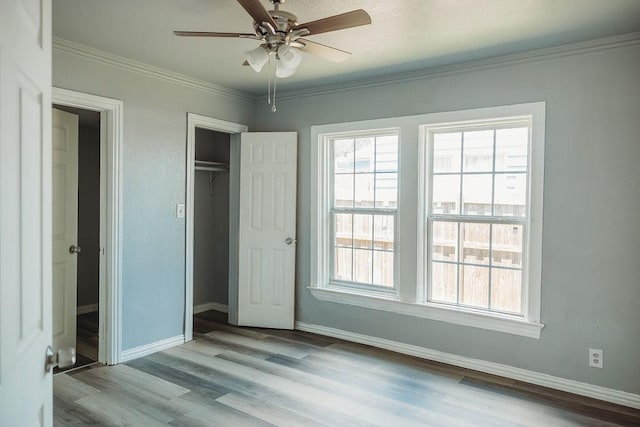 unfurnished bedroom featuring multiple windows, baseboards, wood finished floors, crown molding, and a closet