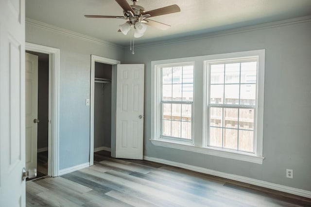 unfurnished bedroom with baseboards, wood finished floors, a closet, crown molding, and ceiling fan