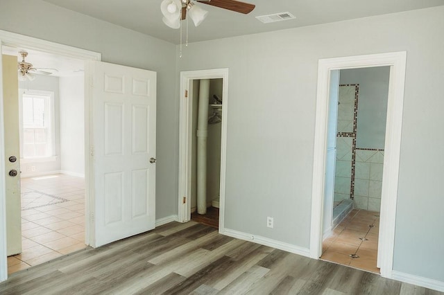 unfurnished bedroom with wood finished floors, a walk in closet, ensuite bath, baseboards, and a closet