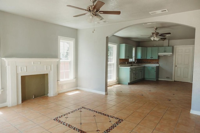 unfurnished living room with ceiling fan, a sink, baseboards, light tile patterned floors, and arched walkways